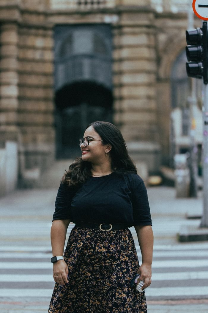 Woman smiling while crossing a city street in front of historic architecture.