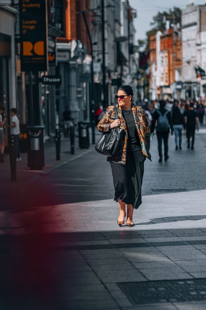 Fashionable woman with sunglasses walks through bustling street in Dublin, Ireland.