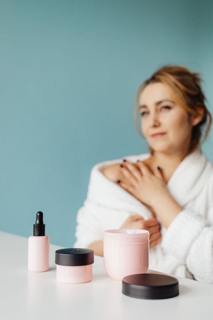 A woman in a bathrobe applies skincare products, emphasizing self-care and beauty.