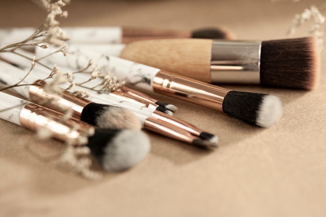 Set of various professional makeup brushes for different cosmetic products with dried flowers on beige surface